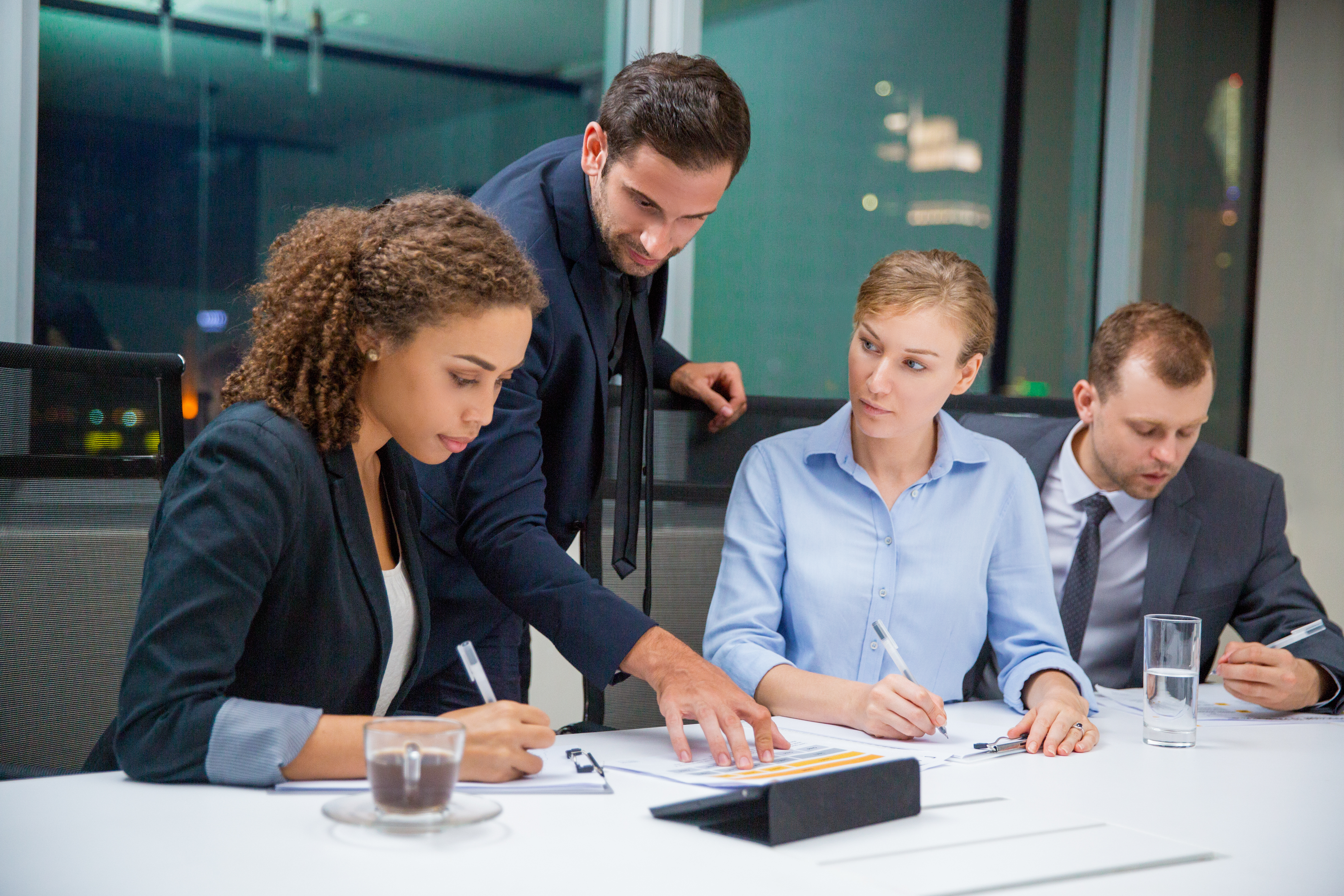 Business people sitting in conference room and discussing business issues. Executive manager standing, pointing to document and explaining his idea to business team